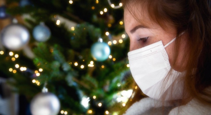 Portrait of a young woman wearing protective face mask and looking sad for Covid-19 with Christmas tree on the background, coronavirus and Christmas concept bokeh