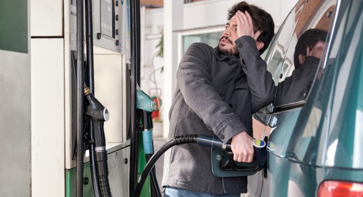 Young man refueling his vehicle while looking worried at the high gas prices at a gas station.