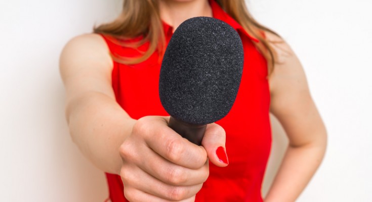 Female reporter with black microphone making interview - journalism and broadcasting concept