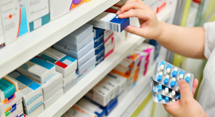 Pharmacist holding medicine box and capsule pack in pharmacy drugstore.